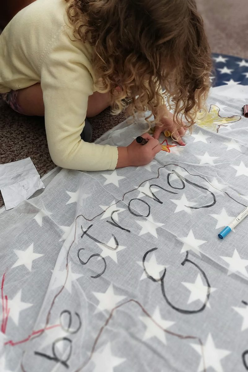 A young girl writing the words 'be strong' on a banner
